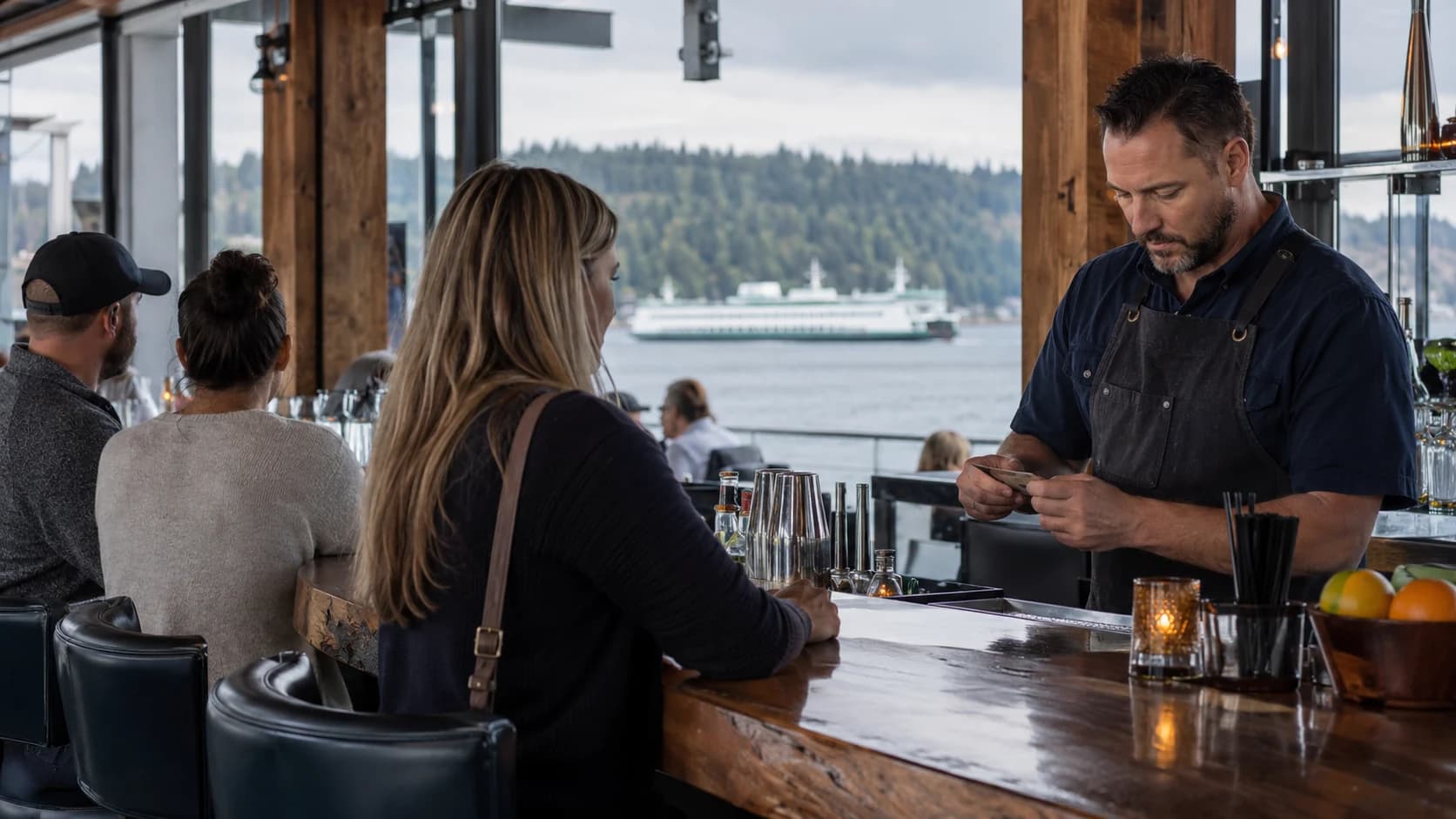 A bartender checking identification in a Washington waterfront restaurant with a Puget Sound ferry.